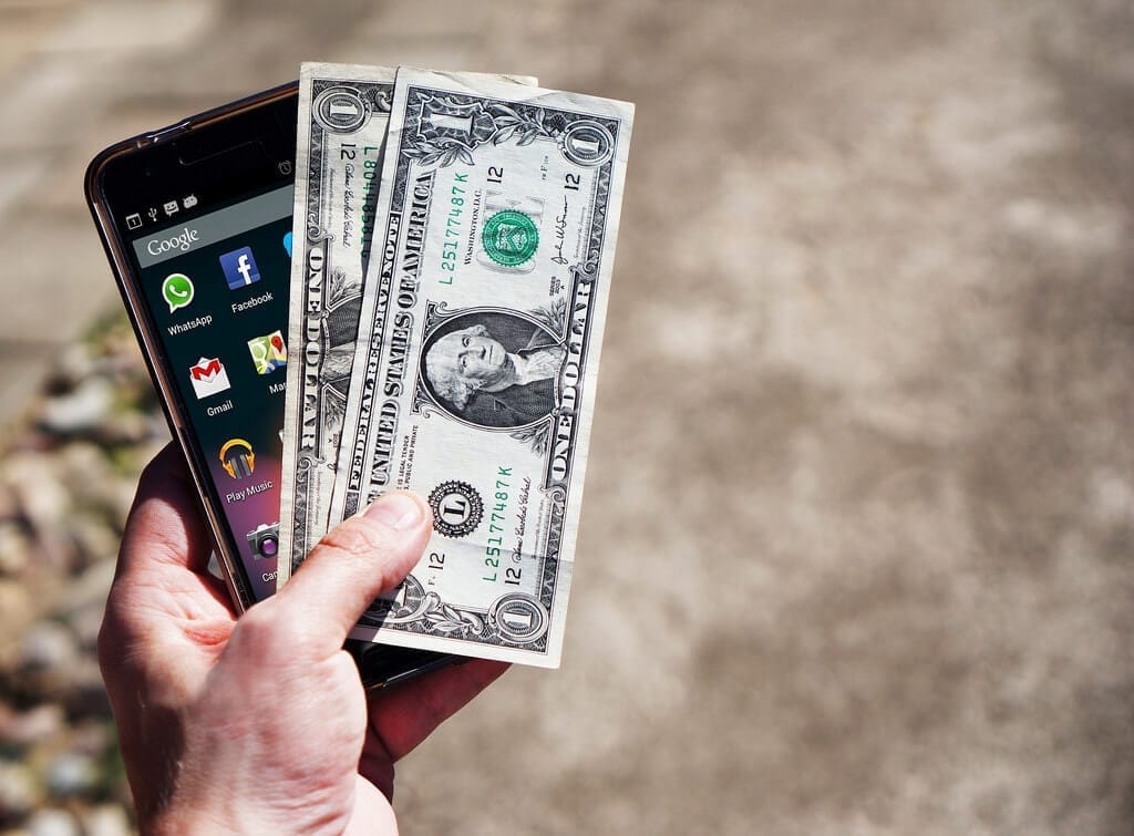 Photo of a person holding a smartphone and two dollar bills