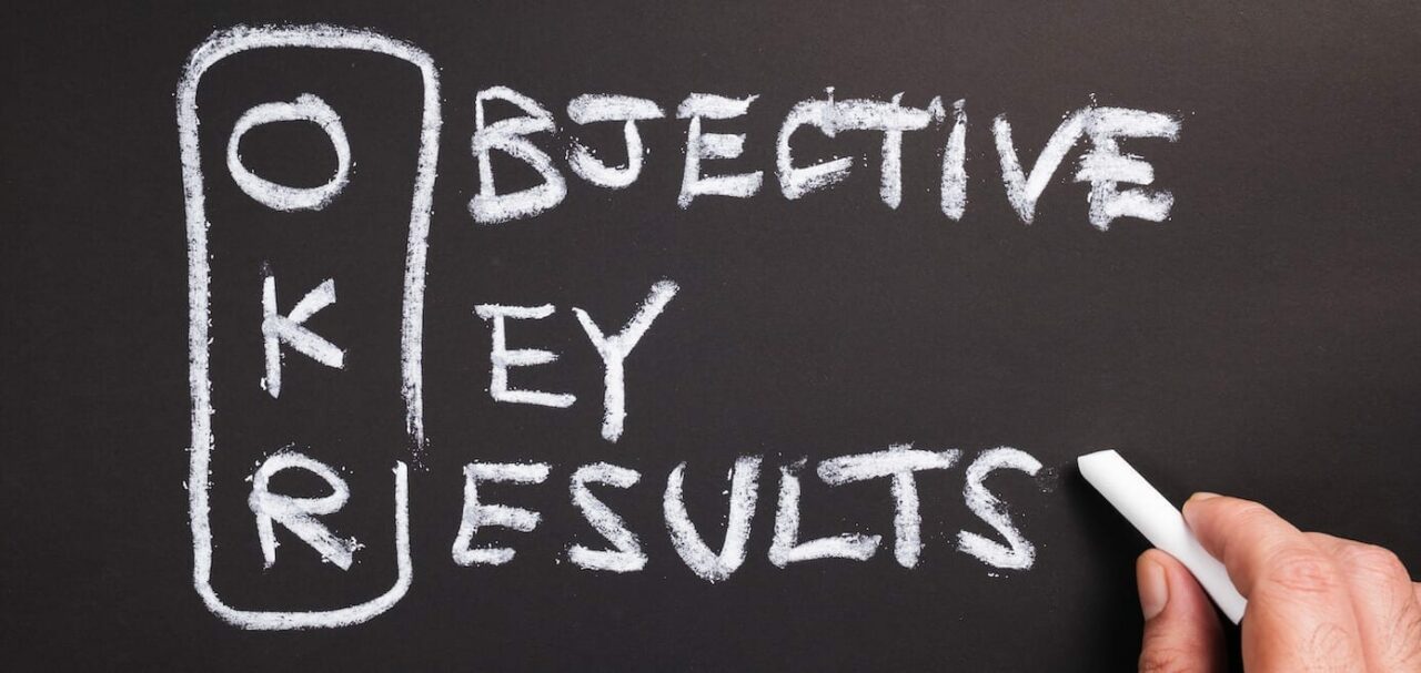 Hand writing text and acronym of OKR (Objective Key Results) on chalkboard